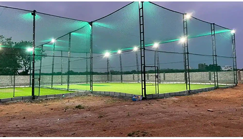Box cricket cage on steel poles with floodlights on an open plot