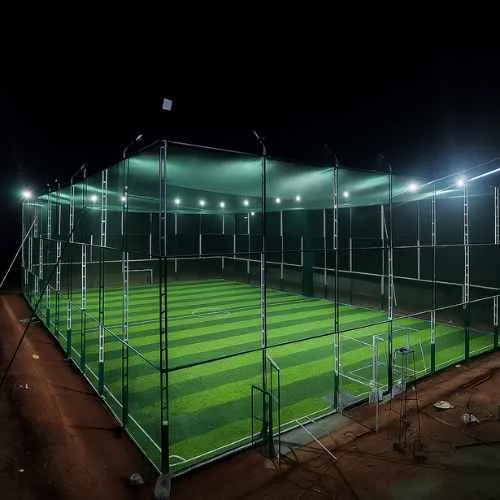 Floodlit box cricket arena enclosed by side and overhead netting at night